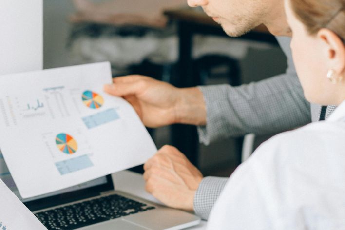 Two business professionals reviewing financial charts and graphs in a modern office setting.